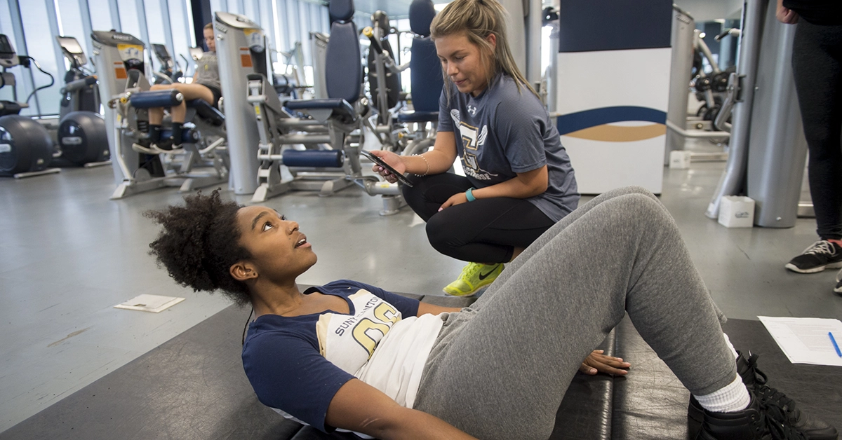 A student does sit-ups while another tracks form and progress in the Fitness Center.