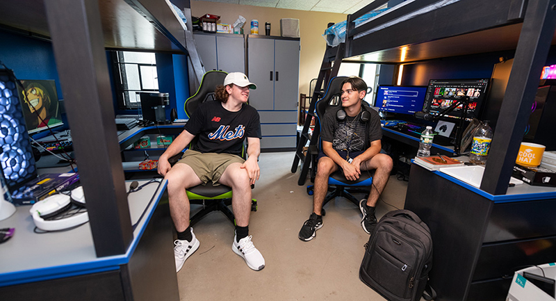 Two students sit in gamer chairs in their new Esports Wing room.