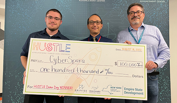 Kyle Meagher, Kambiz Ghazinour and Felix Litvinsky hold a check from HUSTLE.