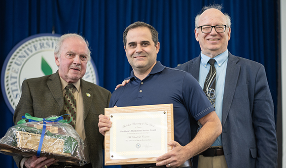 Derek Converse accepts the Presidential Meritorious Service Award from Ronald O'Neill and President Szafran.