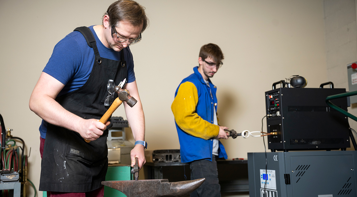 Paul Todd hammers a railroad spike in the Nevaldine Welding Laboratory while Mitch Timerman heats a piece of steel in an induction forge.
