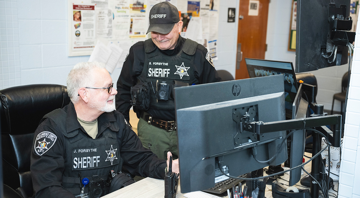 Jeffrey and Steven Forsythe converse around a computer in the Sheriff's Office.