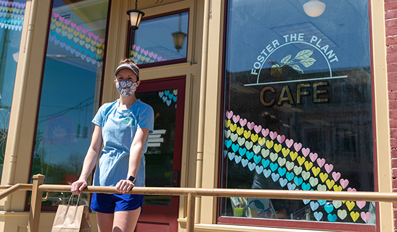 Lynzie Schulte stands in front of her cafe Foster the Plant, wearing a mask.