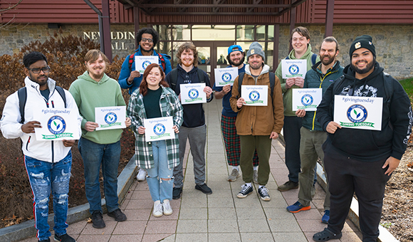 Students holding Giving Tuesday signs stand outside Nevaldine Hall.