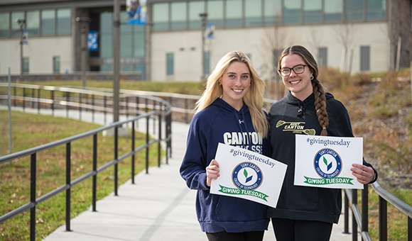 Two nursing students hold Giving Tuesday signs on the new walkway outside French Hall.