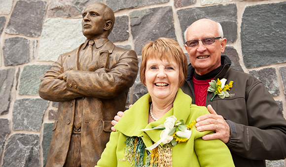 Jill and Terry Martin stand next to the Terry Martin statue outside Roos House.