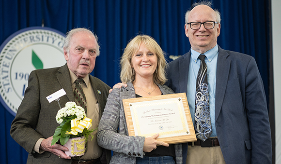 Johanna Lee accepts the Presidential Meritorious Service Award from Ronald O'Neill and President Szafran.