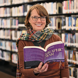 Laini Kavaloski stands in the Southworth Library with her new book Graphic War opened.
