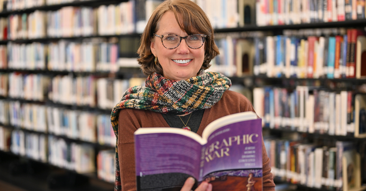 Laini Kavaloski stands in the Southworth Library with her new book Graphic War opened.