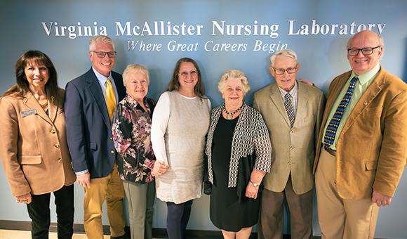 Emeriti guests and SUNY Canton patrons stand with the new signage in Wicks Hall at the rededication of the Virginia McAllister Nursing Laboratory.