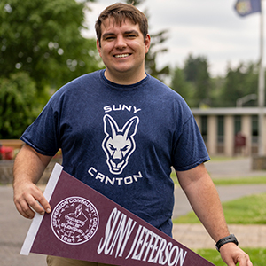 Veteran student Nathaniel Steelman holds a SUNY Jefferson pennant outside French Hall.