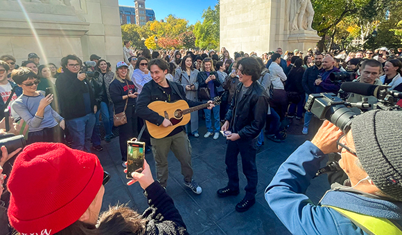 Reed Putman and an acoustic guitarist are surrounded by photographers in New York City's Washington Park.