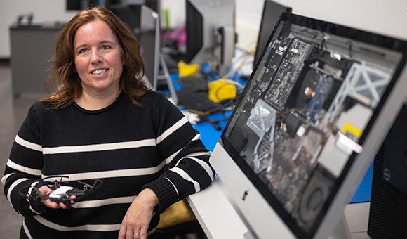 Stacia Smith holds a drone with standing next to an iMac with an open screen.