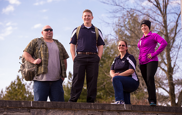 A group of veteran students stand along a stone wall.