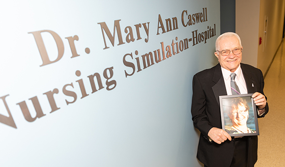 Alson T. Caswell Sr. stands next to the newly unveiled Dr. Mary Ann Caswell Nursing Simulation-Hospital holding a picture of his late wife and the namesake of the new learning area.