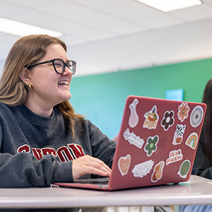 A student with a pink laptop featuring colorful stickers participates in a marketing class.