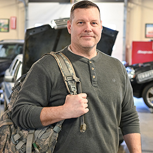 Eric Armstrong holds a camouflaged back pack in the Automotive Technology lab.