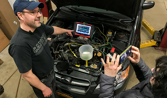 Associate Professor Brandon Baldwin teaches an automotive lab section from his home garage while his wife, Debra Baldwin films him.