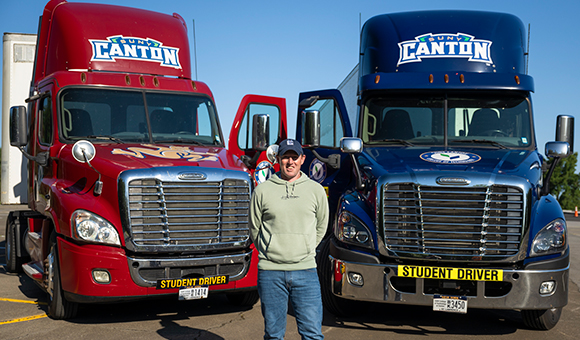 Ryan Harrigan stands between SUNY Canton's CDL training trucks.