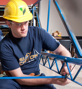 A student with a yellow safety hat constructs a steel bridge.
