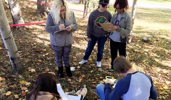 Students discuss and take notes at an outdoor mock crime scene