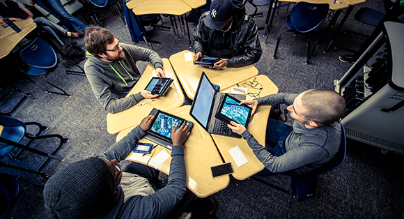 Four students view iPads and laptops in a smart classroom.