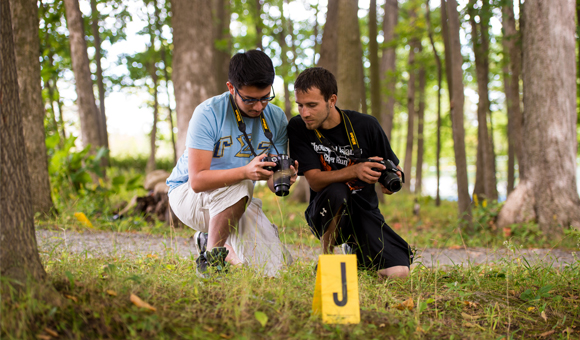 Two students review a photo in the viewfinder at a crime scene.