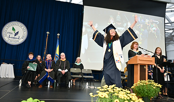 A graduate celebrates with arms up high as they cross the stage.