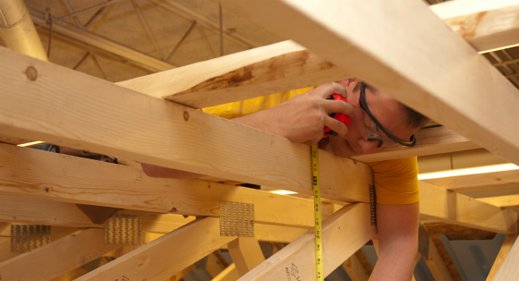 A student measures lumber in the rafters of a mock building.