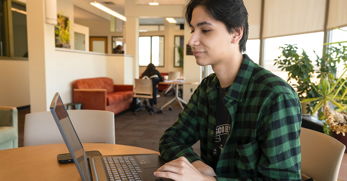 A Cybersecurity students studies on his laptop near a window in Southworth Library.
