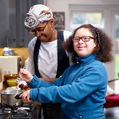A woman assists a girl with special needs in a kitchen.