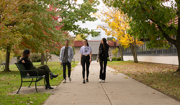 Three students walk along the sidewalk near Nevaldine Hall on a beautiful fall day.