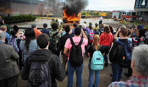 Students watch a mock dorm burn in Roselle Plaza
