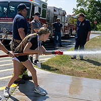 A summer camper sprays a fire hose outside Dana Hall.