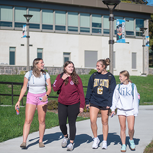 Four students walk together outside French Hall on a bright fall day.
