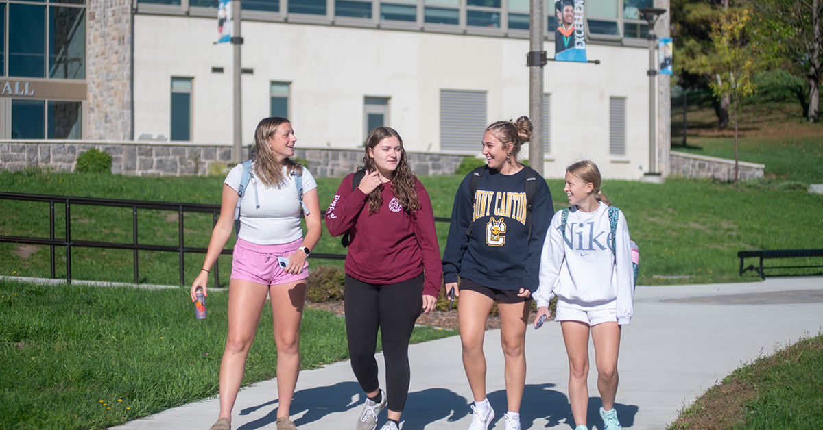 Four students walk together outside French Hall on a bright fall day.