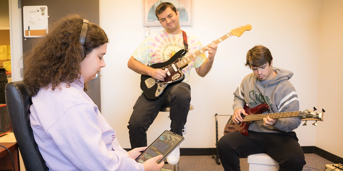 Three students play rock instruments while another records on an iPad.