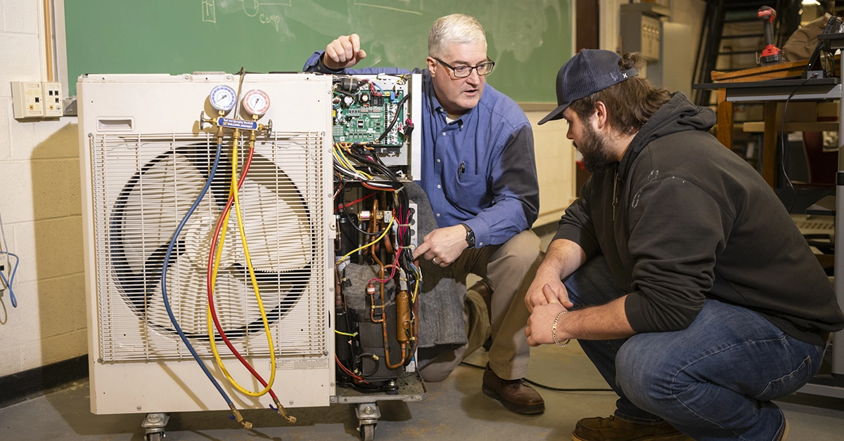 Dean Michael Newtown shows a student the mechanics of a heat pump.