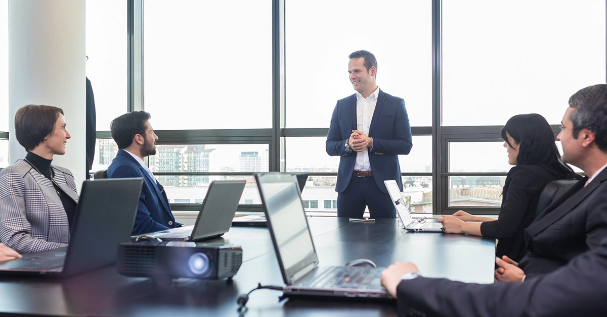 A CEO presents to a board from a high rise room with large windows.