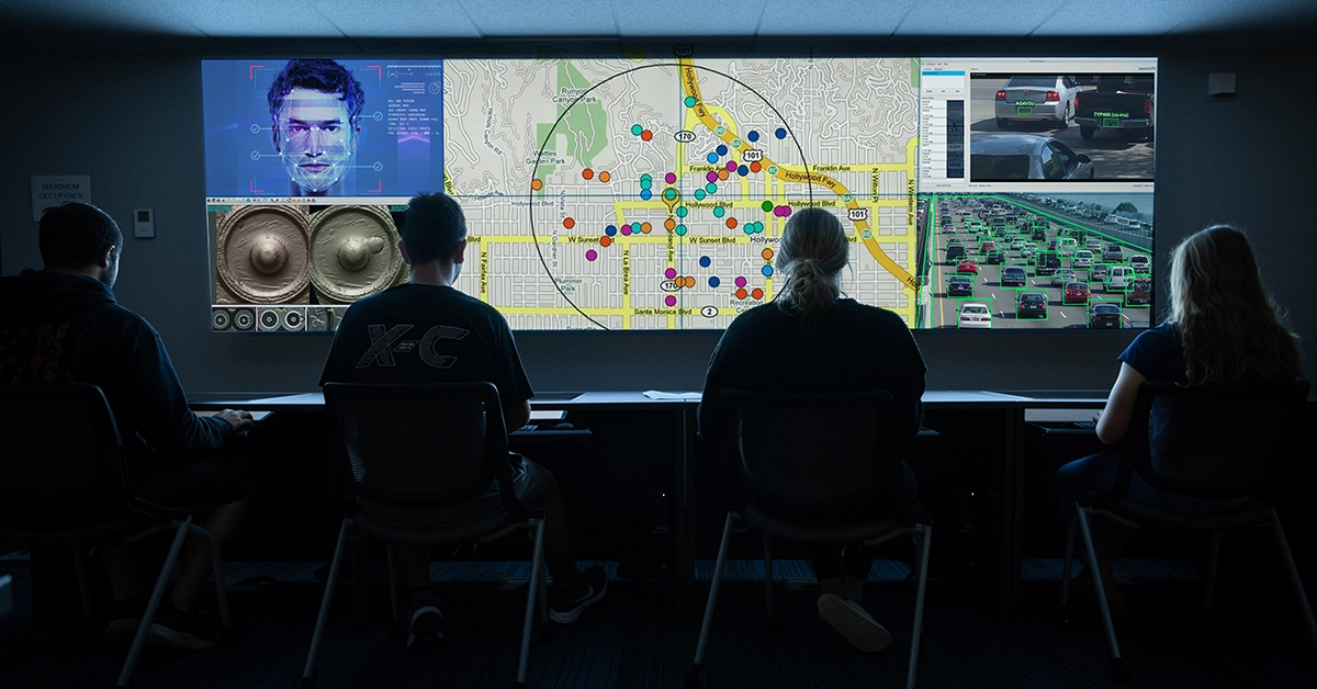 Four silhouetted students sit in front of screen with crime and maps in the Crime Analysis lab.