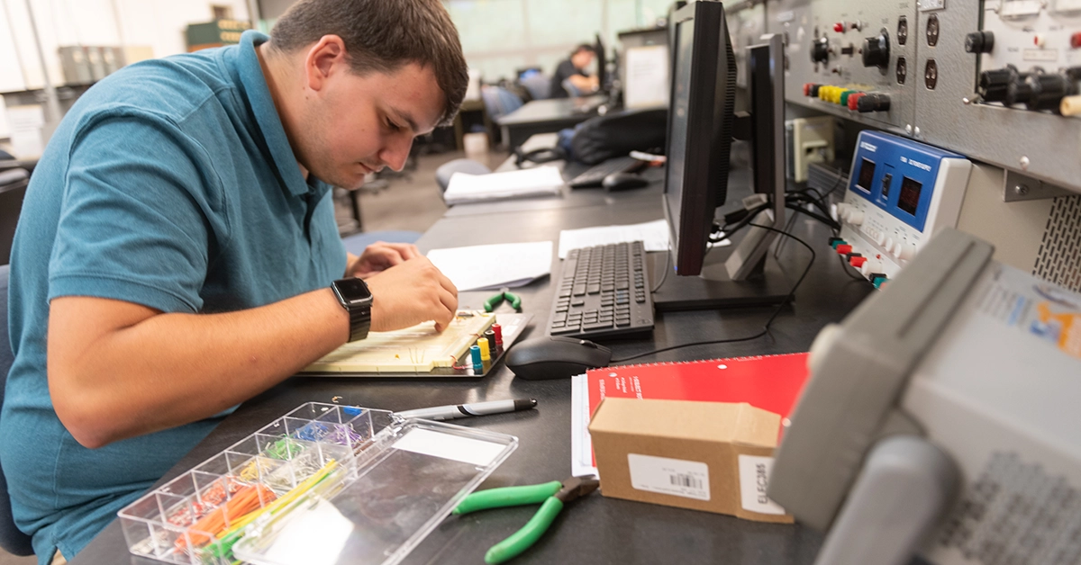 A student wearing a blue shirt works on a motherboard in the Electrical Engineering Technology lab.
