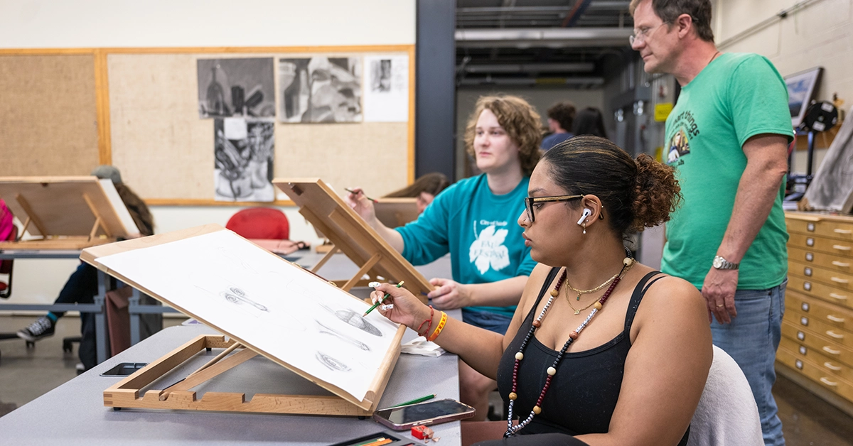 Two students sketch portraits in the GMMD lab while Lecturer Morgan Hastings looks on.