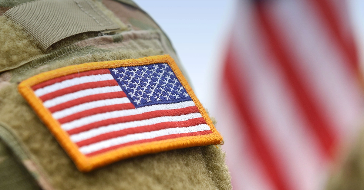 American flag patch on a military uniform. American flag waves in the background.