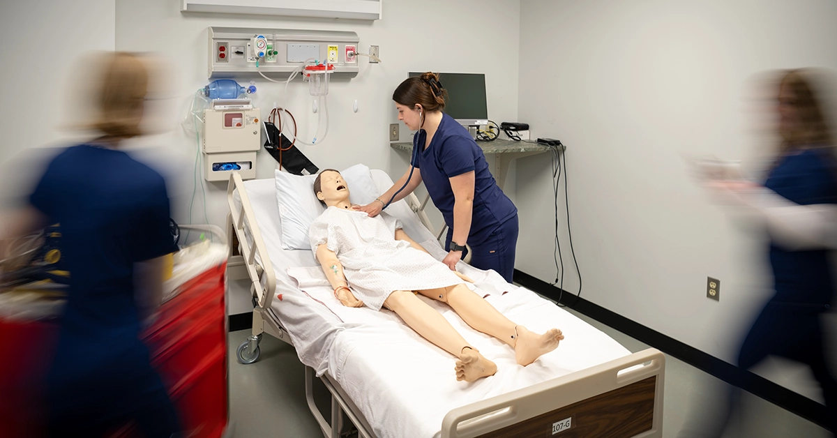 A nurse checks the heart of a simulation dummy while other nurses quickly move on opposite sides.