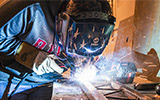 A student welds together portions of a steel bridge.