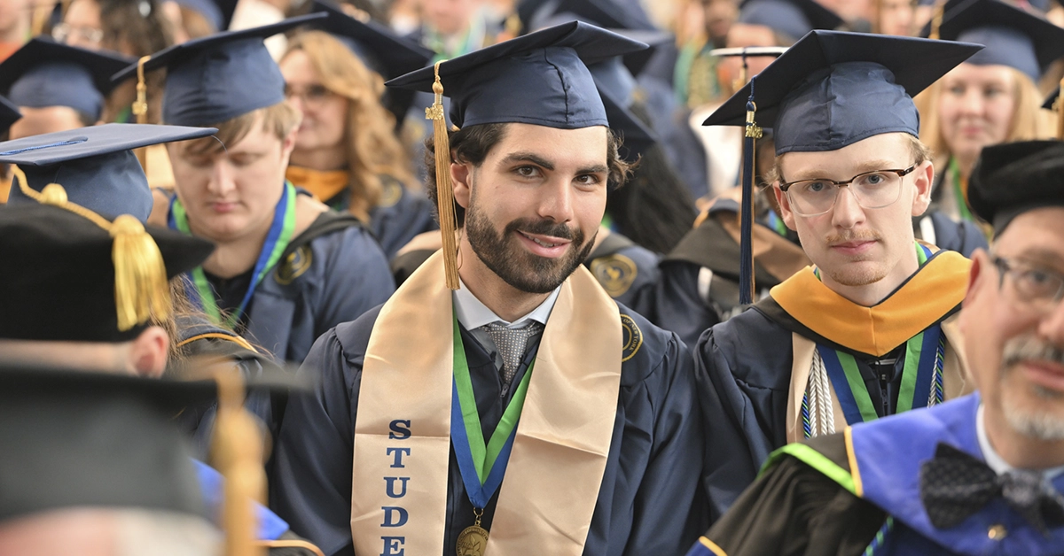 Two graduates with golden Student Athlete sashes smile during the Commencement 2026 ceremony.