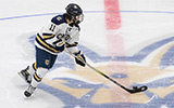 A men's hockey player handles a puck at center ice.