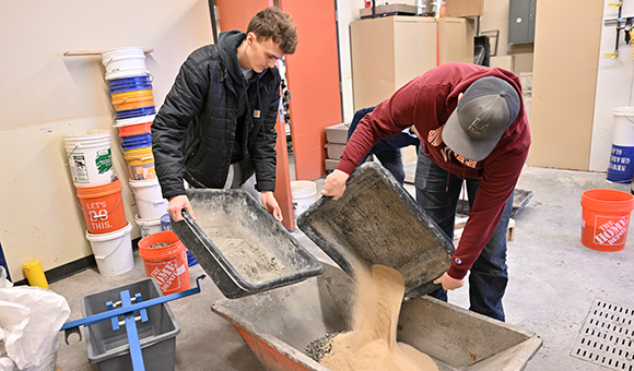 Tim McLellan and Mathew Greene pour sand and cement into a batch of lightweight concrete.