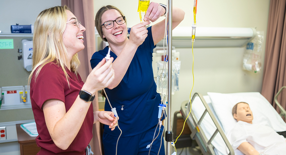 Two students set up an IV unit in the Nursing lab.