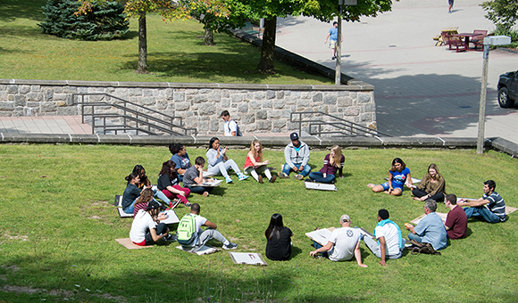 An outdoor class with students sitting in a circle on the grass.